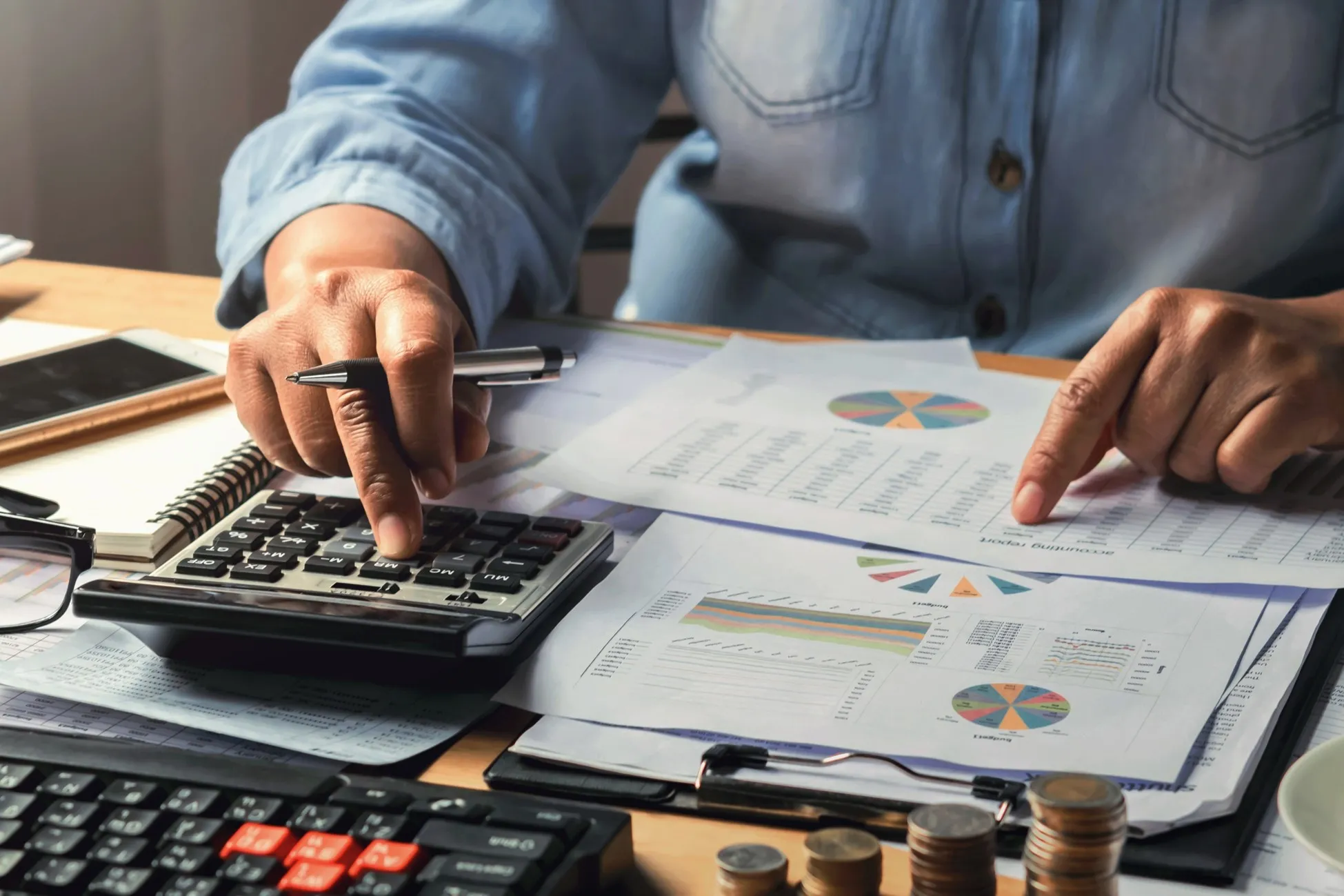 Mãos trabalhando com documentos contábeis, calculadora e relatórios financeiros